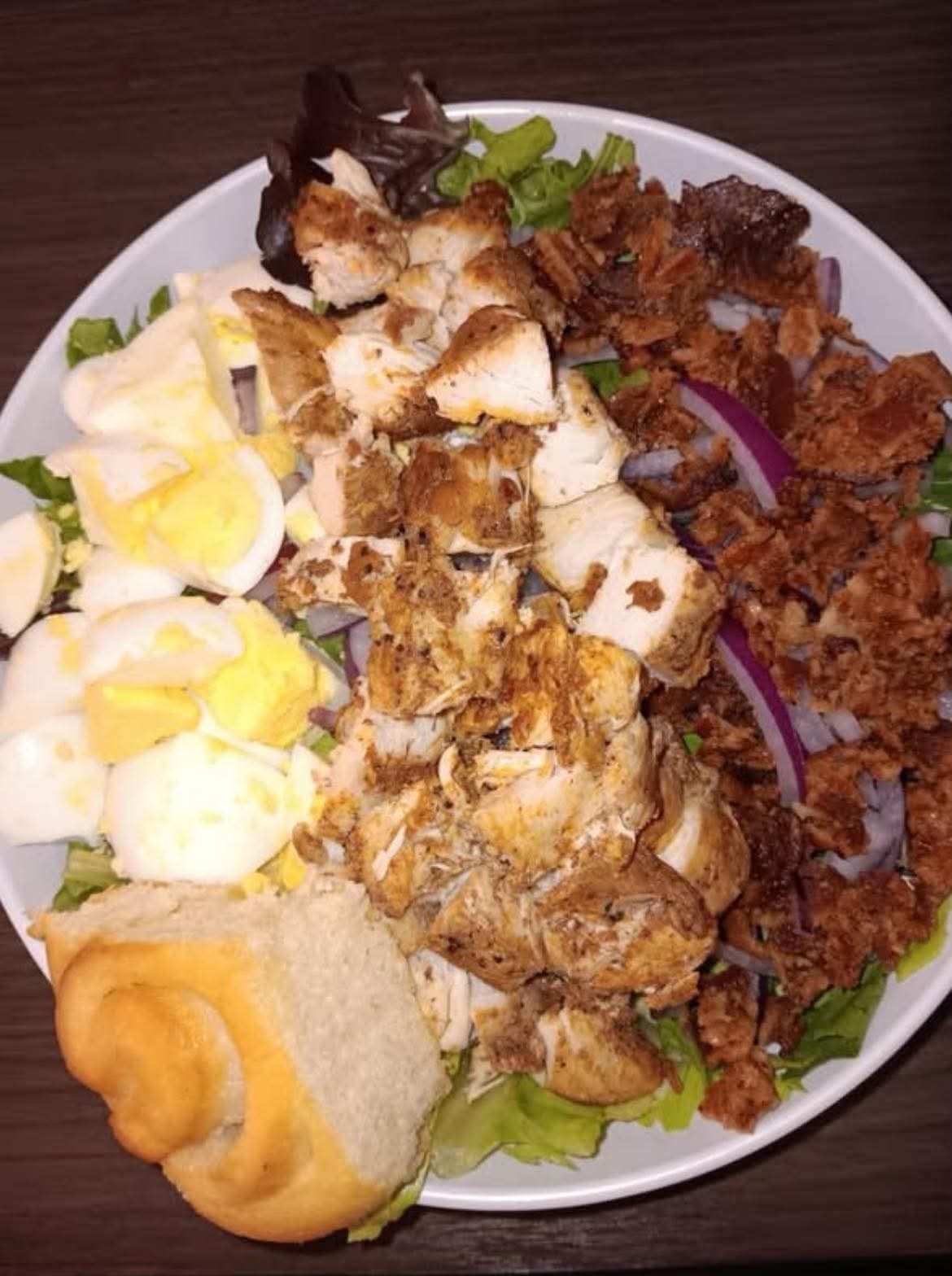 A salad with grilled chicken, bacon, boiled egg and red onion