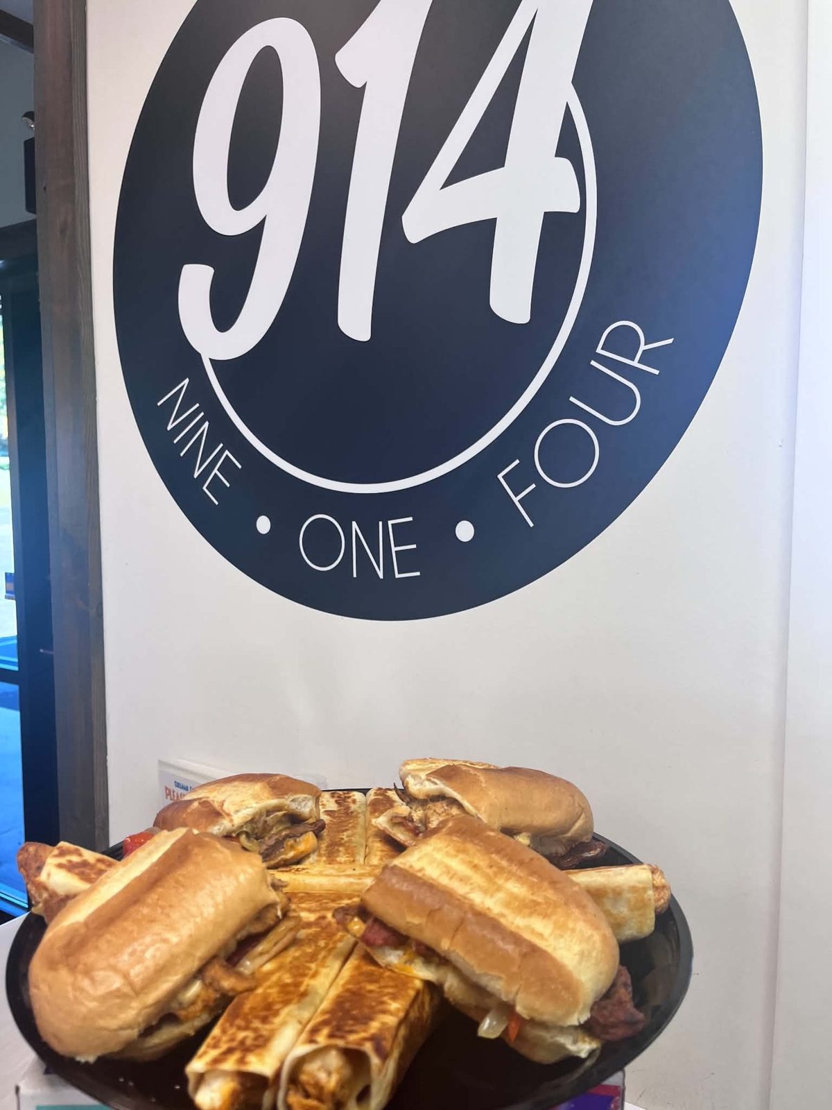 A platter of toasted sandwiches and wraps under the 914 sign